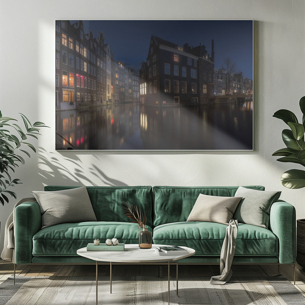 A framed photograph capturing a serene night view of an Amsterdam canal. Traditional Dutch houses with lit windows line the calm water, casting warm reflections under a deep blue twilight sky. Wall Art