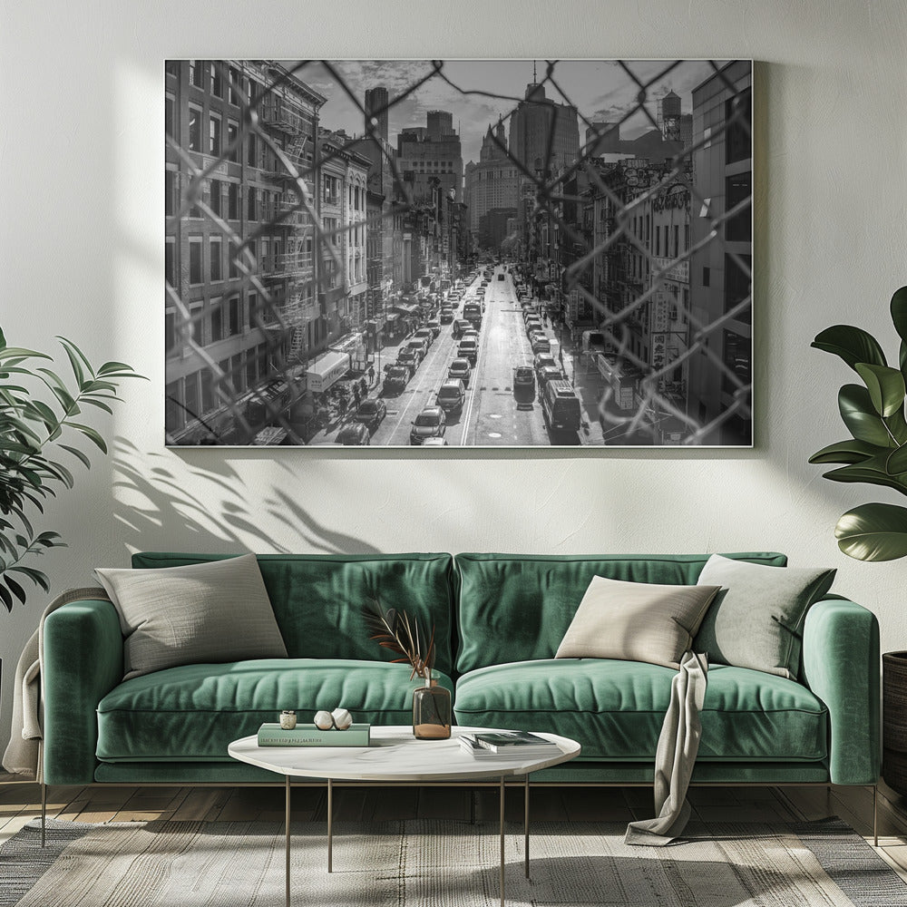 A high-angle, black and white photograph of a bustling New York City street viewed through a chain-link fence. The fence is in the foreground, framing the scene of traffic-filled streets, historic buildings with fire escapes, and skyscrapers in the distance under a cloudy sky. Wall Art