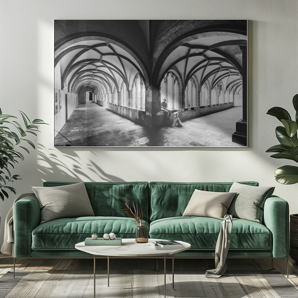 A black and white photograph of a person and their dog sitting in the corner of a Gothic cloister. The stone hallway features a dramatic vaulted ceiling and a long row of arched windows, creating a powerful sense of perspective and light. Decor