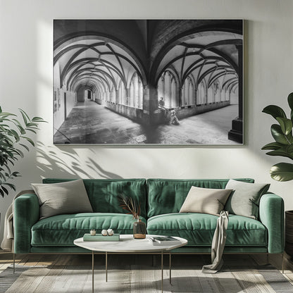A black and white photograph of a person and their dog sitting in the corner of a Gothic cloister. The stone hallway features a dramatic vaulted ceiling and a long row of arched windows, creating a powerful sense of perspective and light. Decor