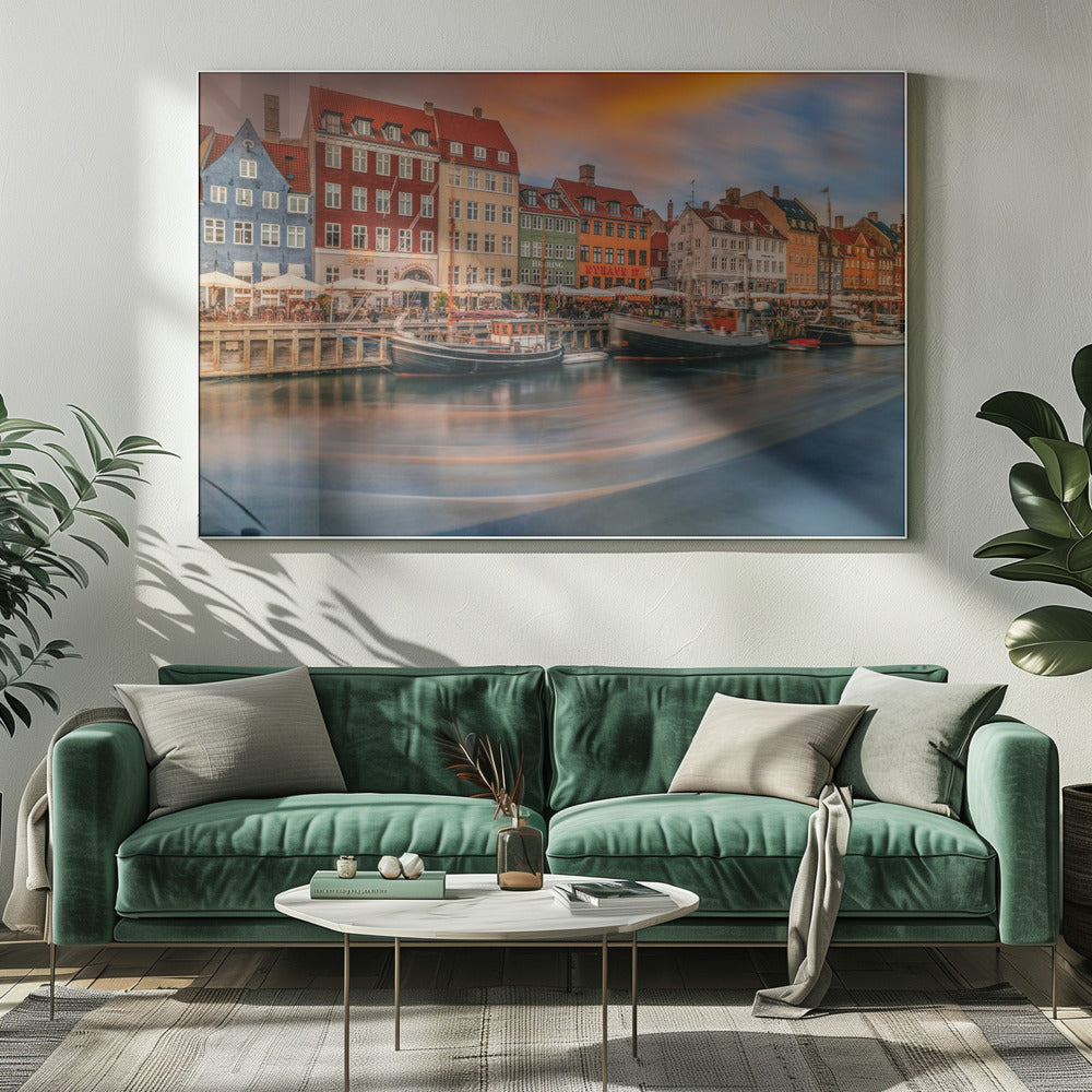 A long-exposure photograph of the colorful Nyhavn harbor in Copenhagen at sunset. Historic, brightly colored buildings line the canal, where two traditional wooden boats are moored. The sky is a dramatic blend of orange and blue, and the water is blurred, showing streaks of reflected light. Decor