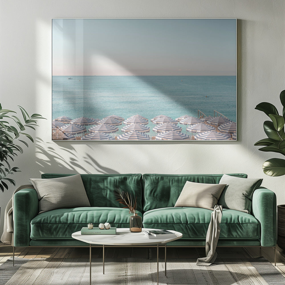 A high-angle photograph of a beach packed with blue and white striped umbrellas, with the turquoise ocean stretching out to a pale blue sky in the background. The entire image is enclosed in a silver frame. Poster