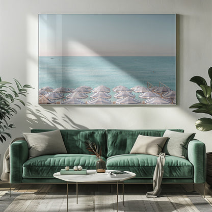 A high-angle photograph of a beach packed with blue and white striped umbrellas, with the turquoise ocean stretching out to a pale blue sky in the background. The entire image is enclosed in a silver frame. Poster