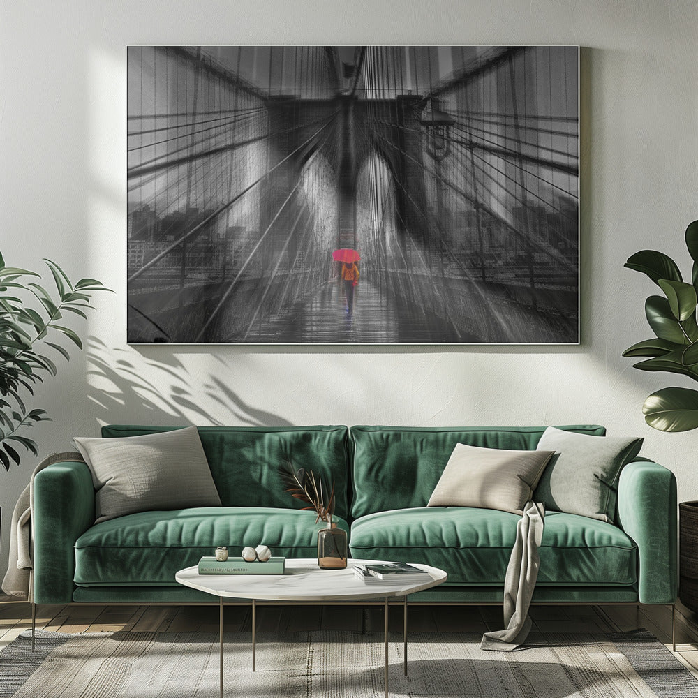 A motion-blurred, black and white photo of the Brooklyn Bridge with a person holding a bright red umbrella walking down the center. The selective color makes the red umbrella the focal point against the dramatic, almost abstract lines of the bridge's cables and arches on a wet, reflective walkway. The image is presented in a silver frame. Wall Art