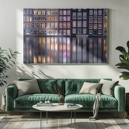 A framed photograph of colorful Amsterdam canal houses at night, their illuminated windows casting vibrant, shimmering reflections on the water below. Artwork