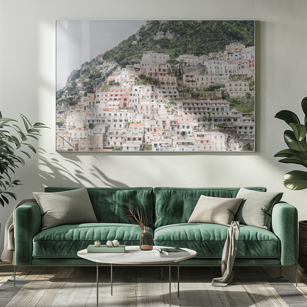 Photograph of the iconic cliffside village of Positano on the Amalfi Coast, showcasing a dense cascade of white, pink, and peach buildings down a lush green mountain under an overcast sky. The image is presented within a silver picture frame. Artwork