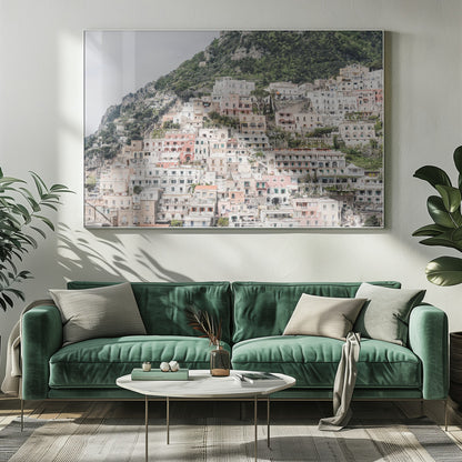 Photograph of the iconic cliffside village of Positano on the Amalfi Coast, showcasing a dense cascade of white, pink, and peach buildings down a lush green mountain under an overcast sky. The image is presented within a silver picture frame. Artwork