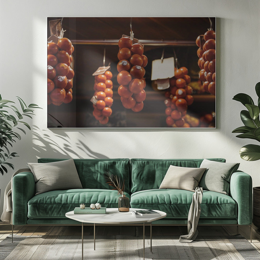 A close-up, warm-toned photograph of several bunches of ripe red tomatoes hanging from hooks in a row, likely at a market or in a pantry. The background is dark and out of focus, highlighting the vibrant produce. Poster