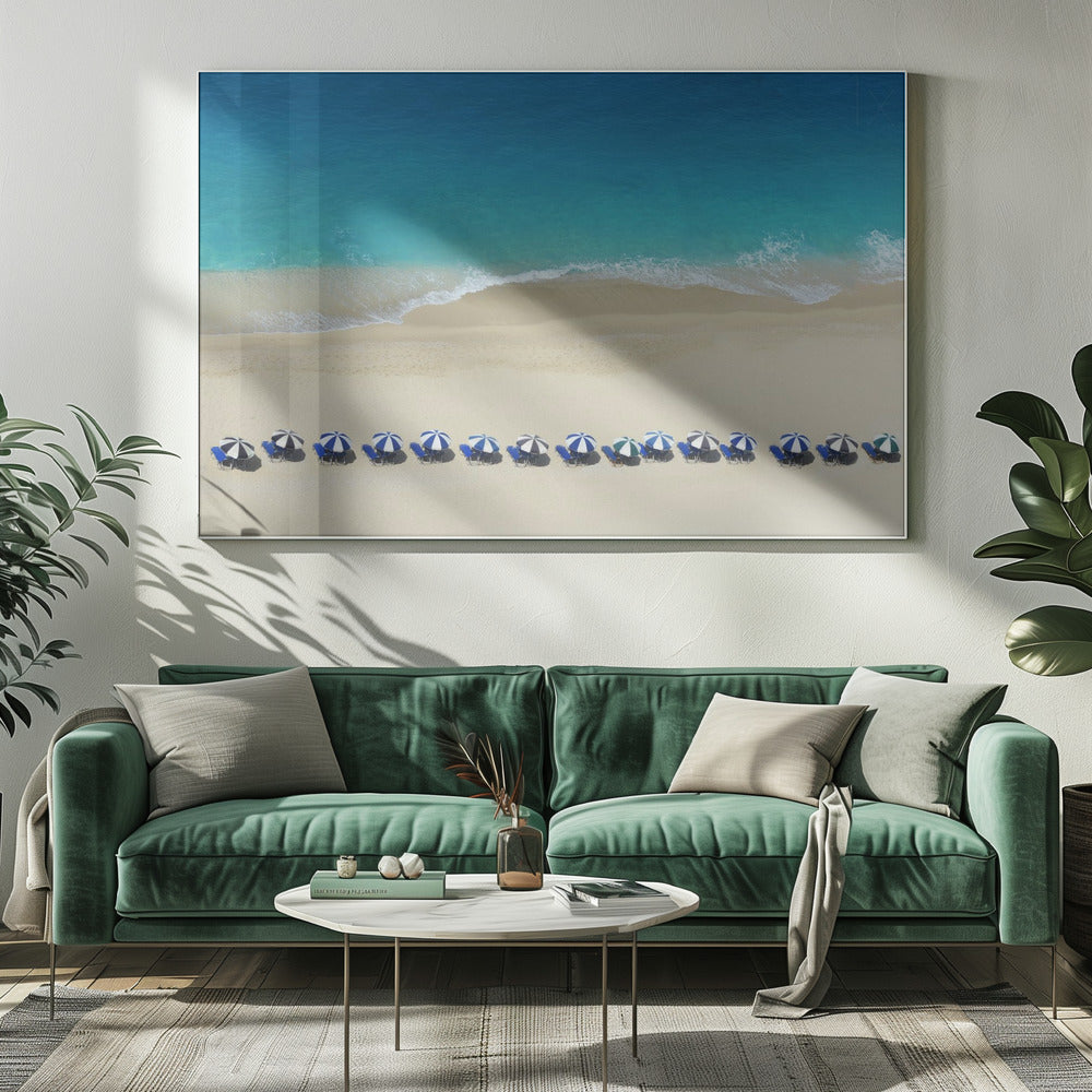 An aerial view of a pristine sandy beach with vibrant turquoise ocean waves gently lapping the shore. A long, neat row of blue and white striped beach umbrellas stands along the sand, creating a serene and orderly coastal scene, all enclosed within a silver frame. Artwork