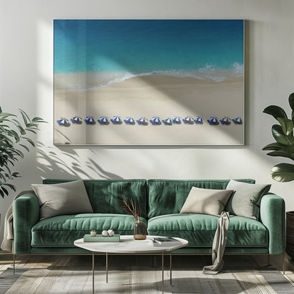 An aerial view of a pristine sandy beach with vibrant turquoise ocean waves gently lapping the shore. A long, neat row of blue and white striped beach umbrellas stands along the sand, creating a serene and orderly coastal scene, all enclosed within a silver frame. Artwork