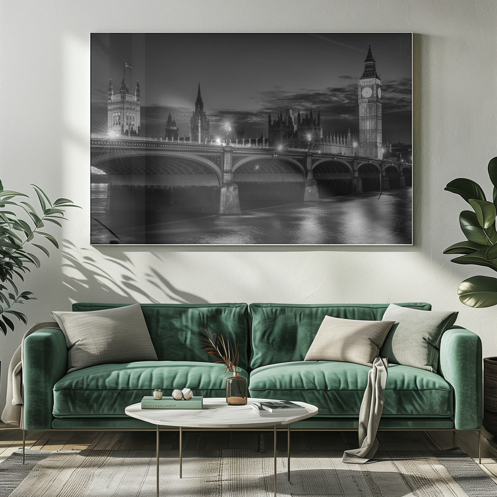 A framed, black and white nighttime photograph of Westminster Bridge in London. The iconic Houses of Parliament and the glowing Big Ben clock tower stand prominently in the background against a dark, cloudy sky. The streetlights on the bridge create starburst effects, and their reflections shimmer on the surface of the River Thames in the foreground. Poster