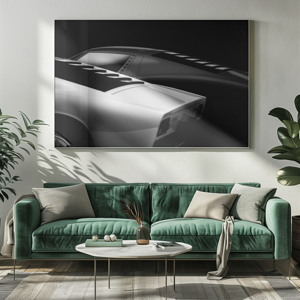 A dramatic black and white studio photograph showcasing the sleek, curved lines of two classic sports cars, with a white car in the foreground and a dark one in the background, set against a black backdrop. Wall Art