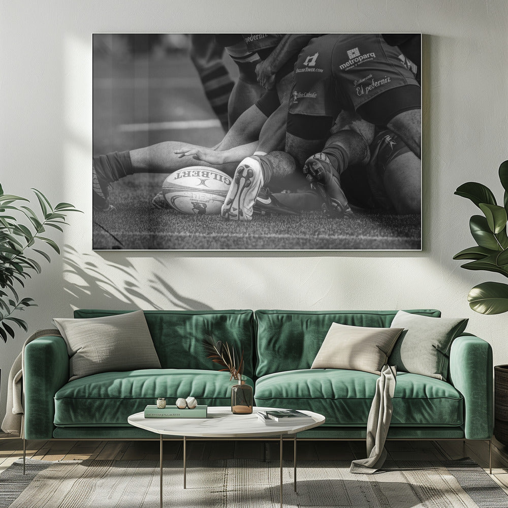 A dynamic black and white, low-angle photograph capturing the intensity of a rugby ruck. A Gilbert rugby ball sits on the turf in the foreground, surrounded by a tangle of players' muscular legs, arms, and cleats, conveying the raw power and action of the sport. Wall Art