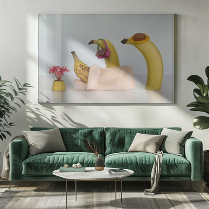 A whimsical still life photo featuring three bananas personified as a family or friends. One overripe, spotted banana lies down, covered by a pink towel, while another banana with a tiny pink purse and a third with a small hat seem to be visiting. A small vase with pink flowers sits nearby on the white surface. Poster