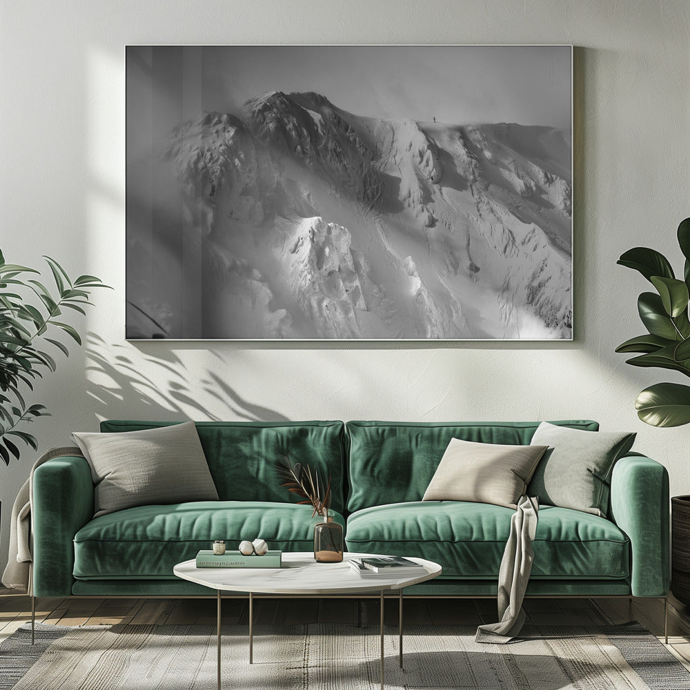 A dramatic black and white photograph of a person standing alone on the ridge of a massive, snow-covered mountain, emphasizing the scale and solitude of the vast, rugged landscape, all presented in a silver frame. Wall Art