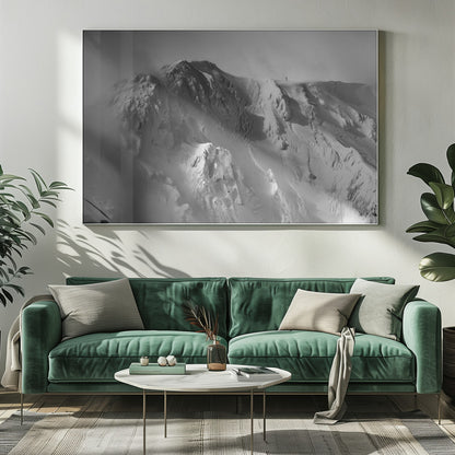 A dramatic black and white photograph of a person standing alone on the ridge of a massive, snow-covered mountain, emphasizing the scale and solitude of the vast, rugged landscape, all presented in a silver frame. Wall Art