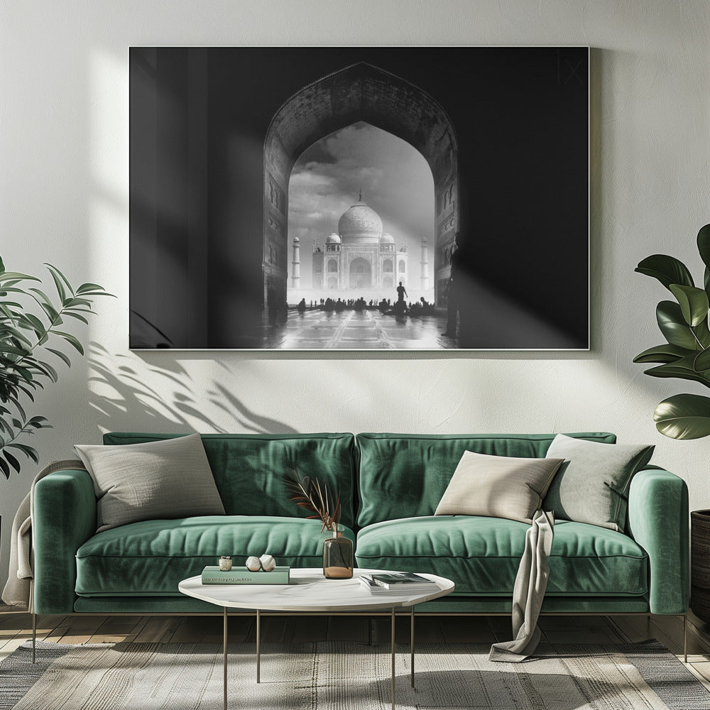 A dramatic black and white photograph of the Taj Mahal seen through a large, dark archway which frames the view. The iconic mausoleum is in the distance under a cloudy sky, and the silhouettes of many people are scattered on the wet, reflective ground in the foreground. Decor