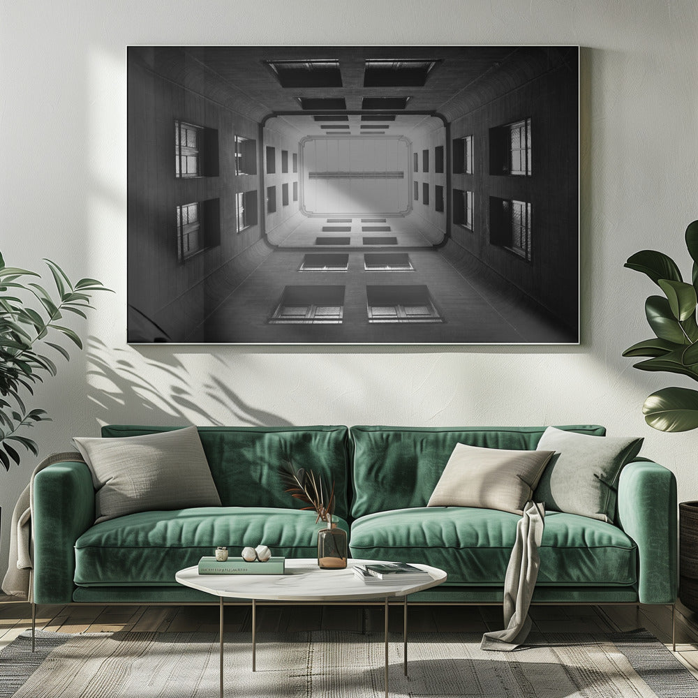 A symmetrical, black and white photograph looking directly up from the base of a building's interior courtyard. The dark walls rise up, lined with rows of windows, creating a powerful sense of perspective that draws the eye to the bright rectangle of the sky or a skylight at the top. The image is enclosed in a simple silver frame. Poster