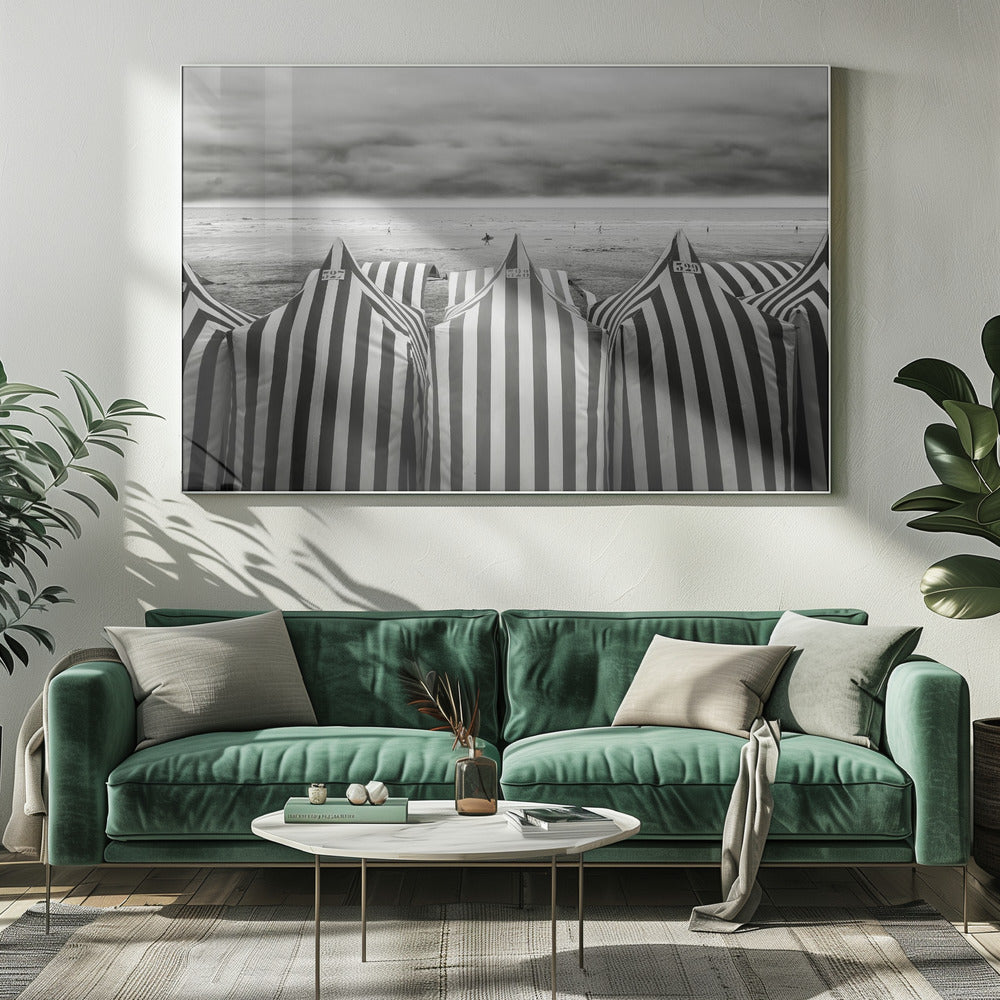 A framed, black and white photograph of striped beach tents on a cloudy day, with the ocean and distant surfers in the background. Print