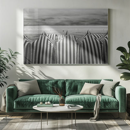 A framed, black and white photograph of striped beach tents on a cloudy day, with the ocean and distant surfers in the background. Print