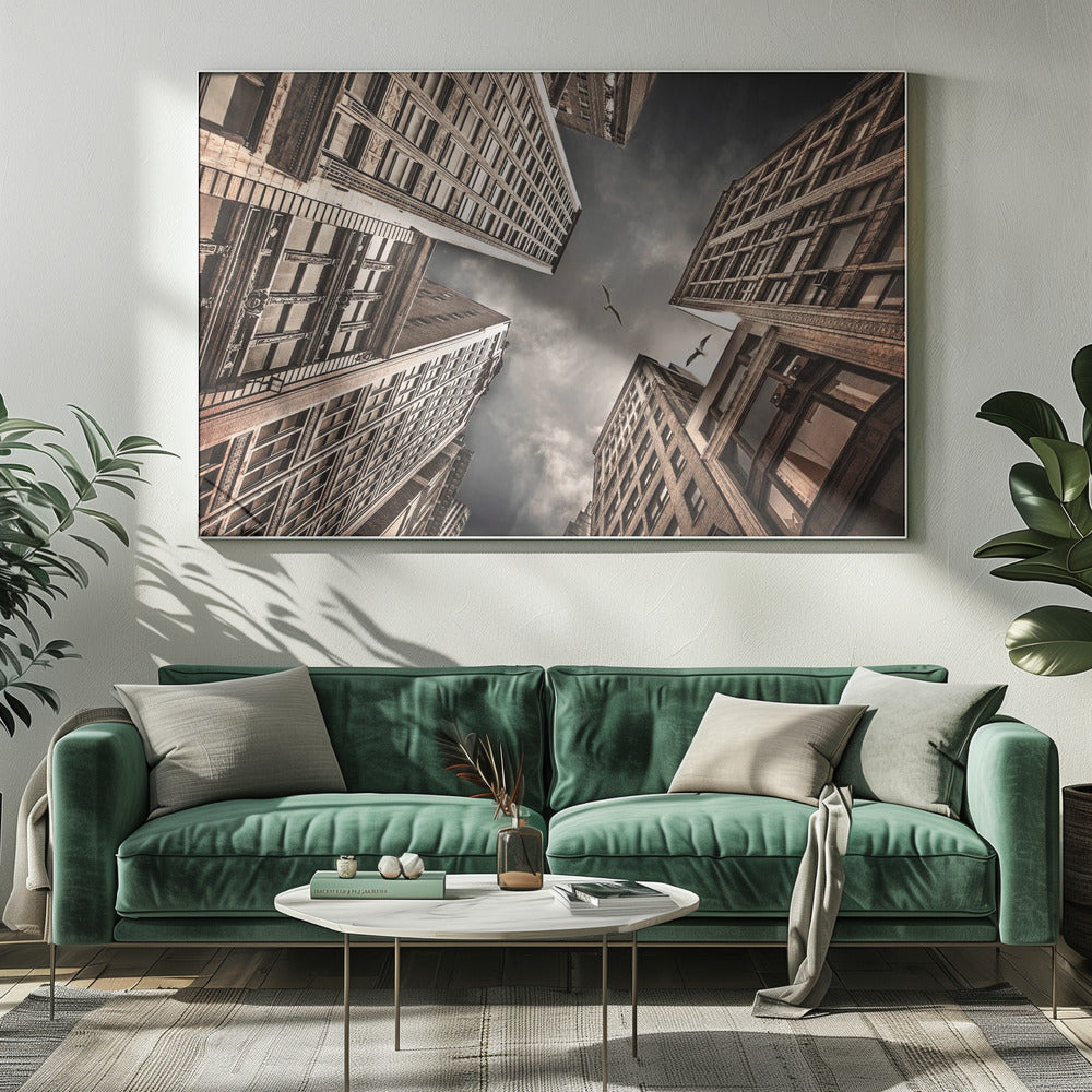 A dramatic, low-angle photograph looking up at the sky between several tall, sepia-toned skyscrapers that converge towards the center. Two birds are seen flying in the moody, dark grey sky. The image has a vintage feel and is presented in a silver frame. Wall Art