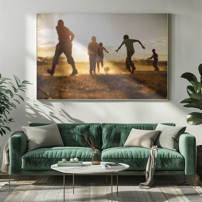 A low-angle, warmly lit photograph of five children silhouetted against a bright sunset as they play soccer on a dusty field, kicking up clouds of dust in the golden light. Decor
