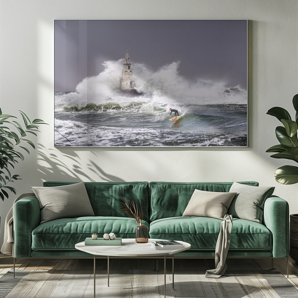 A framed photograph of a surfer in a black wetsuit riding a wave in a stormy sea. In the background, massive white waves crash against an old white lighthouse under a grey, overcast sky. Artwork