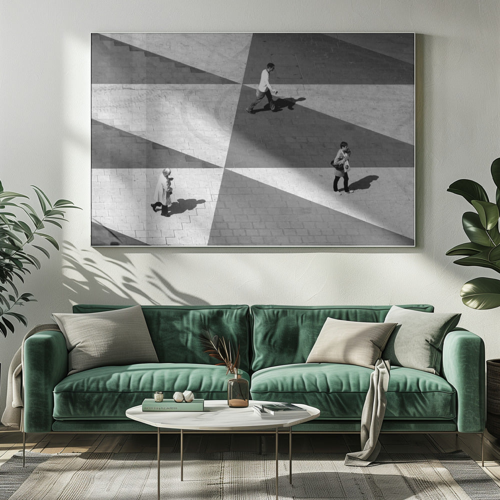 A high-angle, black and white photograph capturing three people walking across a paved plaza, their paths intersecting with a dramatic geometric pattern of light and shadow. The strong sunlight creates large, sharp-edged triangles of shade, isolating each figure in the composition, which is enclosed in a silver frame. Decor