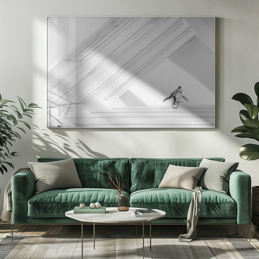 A minimalist black and white photograph in a silver frame, featuring a lone BMX rider performing a trick on the back wheel inside a stark, modern building with strong diagonal architectural lines. Poster