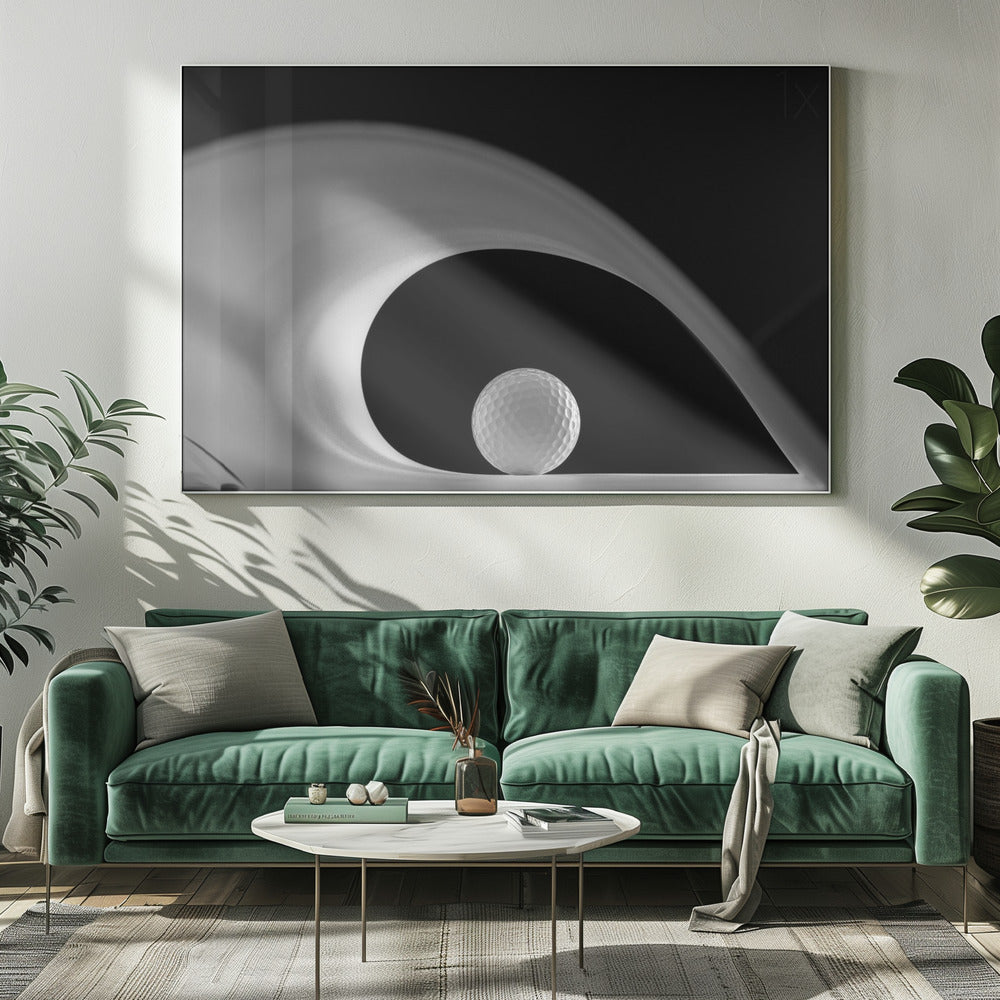 A dramatic black and white still life photo featuring a golf ball set against a stark black background. A large, abstract white shape swirls gracefully over the ball, creating a dynamic, wave-like composition. The image is presented within a silver frame. Decor