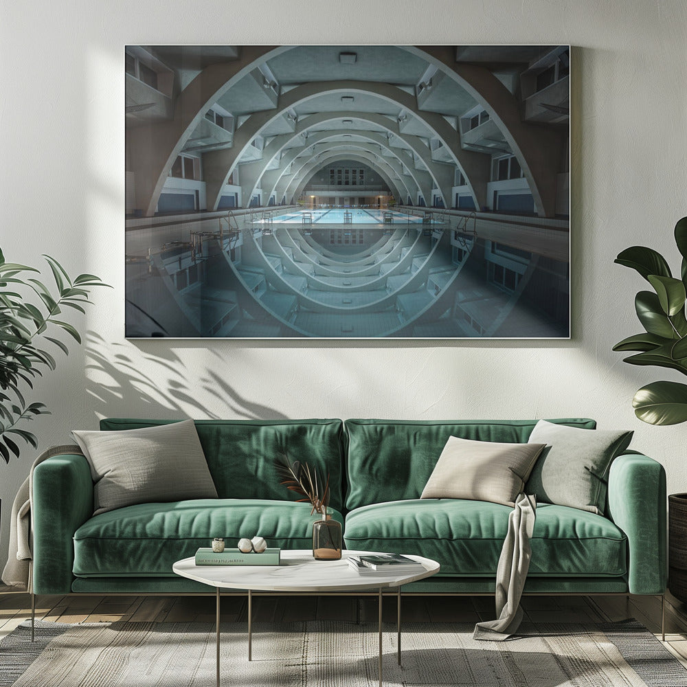 An atmospheric photograph of an empty indoor swimming pool with remarkable Brutalist-style architecture. A series of large, repeating concrete arches span the length of the pool, creating a tunnel-like effect. The arches and lights are perfectly reflected in the still, blue water, forming a symmetrical, eye-like shape. Decor