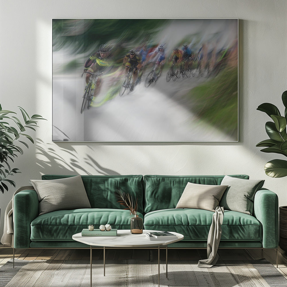 A dynamic, motion-blurred photograph of a group of cyclists in a race, captured with a slow shutter speed to create streaks of color and a sense of high speed. The lead cyclist in a yellow and black jersey is the most defined figure, leaning into a turn on a grey road flanked by blurry green foliage. The entire image is enclosed in a silver frame. Decor