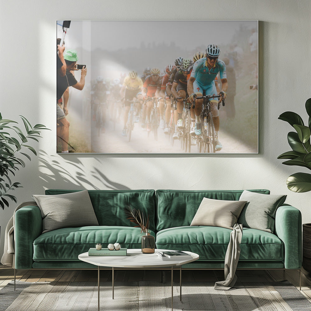 A framed photograph of a peloton of professional cyclists racing down a dusty dirt road. The lead cyclist is in sharp focus, wearing a bright turquoise uniform and a helmet, with other racers in yellow and red jerseys blurred behind him. A spectator on the left is taking a photo with a smartphone. Poster