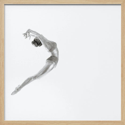 A minimalist black and white photograph of a graceful dancer frozen in mid-air, her body arched backward in an elegant C-shape against a stark white background. The artwork is presented in a light wood frame. Decor