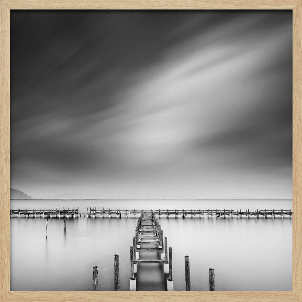 A framed, square black and white long-exposure photograph of a dilapidated wooden pier extending into calm, misty water. The sky is filled with soft, streaked clouds, creating a serene and melancholic mood. Wall Art