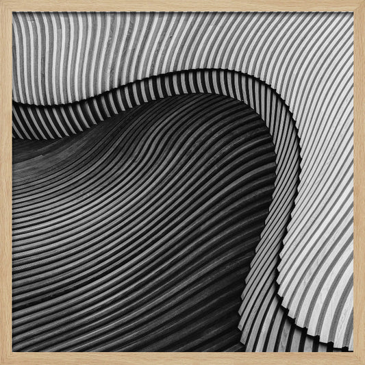 A square, black and white abstract photograph in a light wood frame. The image features layers of flowing, curved surfaces with parallel grooves, creating a strong sense of texture and depth. Lighter, striped layers with vertical lines curve over a darker, undulating section, resembling waves or sculpted wood, drawing the eye into a central dark crevice. Decor