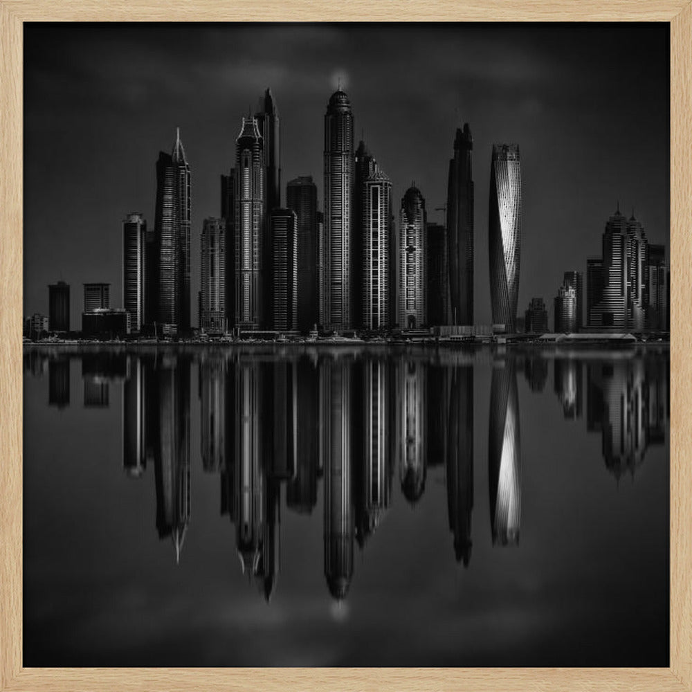 A dramatic black and white photograph of a modern city skyline at night, its towering skyscrapers perfectly reflected in the calm water below, all enclosed within a light brown wooden frame. Print