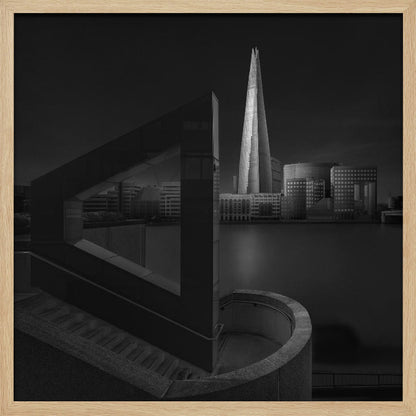 A dramatic black and white architectural photograph of the London skyline at night. The illuminated Shard skyscraper stands tall in the background across a dark river. The foreground features strong geometric shapes, including a large triangular structure and a curved concrete staircase, creating a layered and modern composition. Print