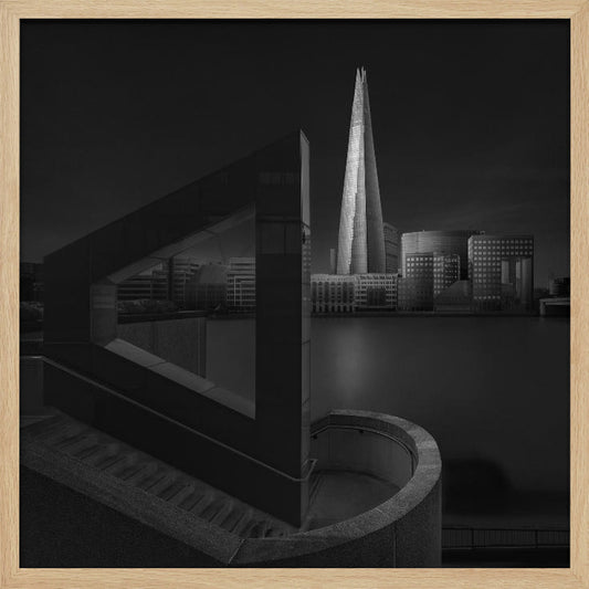 A dramatic black and white architectural photograph of the London skyline at night. The illuminated Shard skyscraper stands tall in the background across a dark river. The foreground features strong geometric shapes, including a large triangular structure and a curved concrete staircase, creating a layered and modern composition. Print