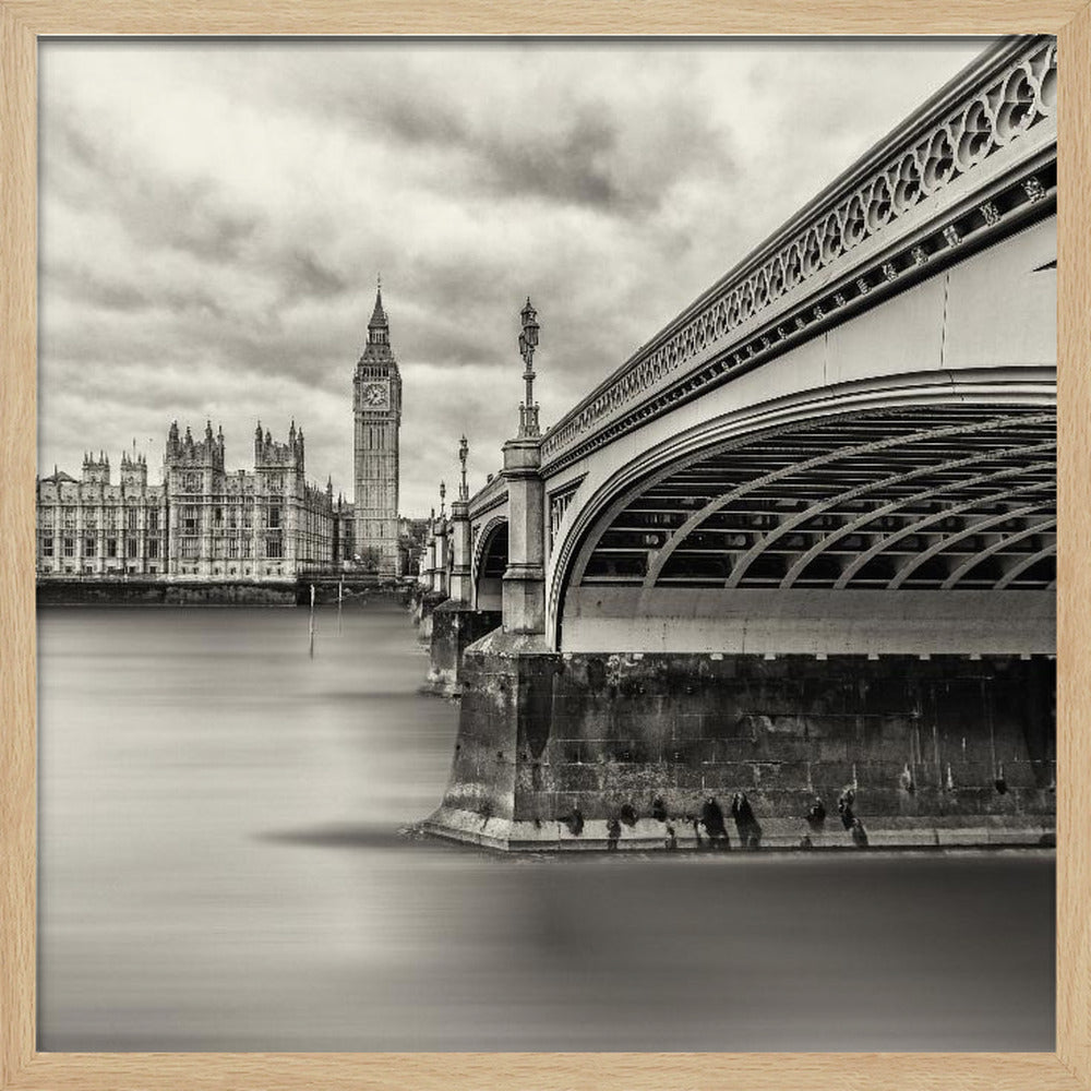 A framed, long-exposure, black and white photograph of London. The image shows Westminster Bridge from a low angle on the right, with the River Thames appearing smooth and misty. In the background on the left are the Houses of Parliament and the Big Ben clock tower under a cloudy sky. Wall Art