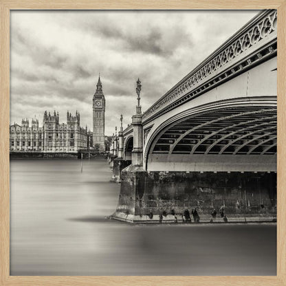 A framed, long-exposure, black and white photograph of London. The image shows Westminster Bridge from a low angle on the right, with the River Thames appearing smooth and misty. In the background on the left are the Houses of Parliament and the Big Ben clock tower under a cloudy sky. Wall Art