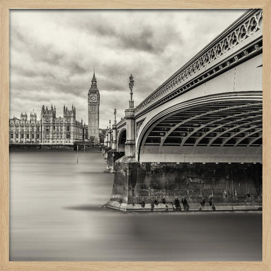 A framed, long-exposure, black and white photograph of London. The image shows Westminster Bridge from a low angle on the right, with the River Thames appearing smooth and misty. In the background on the left are the Houses of Parliament and the Big Ben clock tower under a cloudy sky. Wall Art