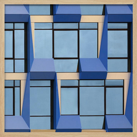 A framed abstract architectural photograph showing a repeating pattern of a modern building's facade. The image features geometric, three-dimensional blue elements surrounding light blue windows with black frames, all set against horizontal cream-colored bands. The entire piece is presented within a light wood frame. Print