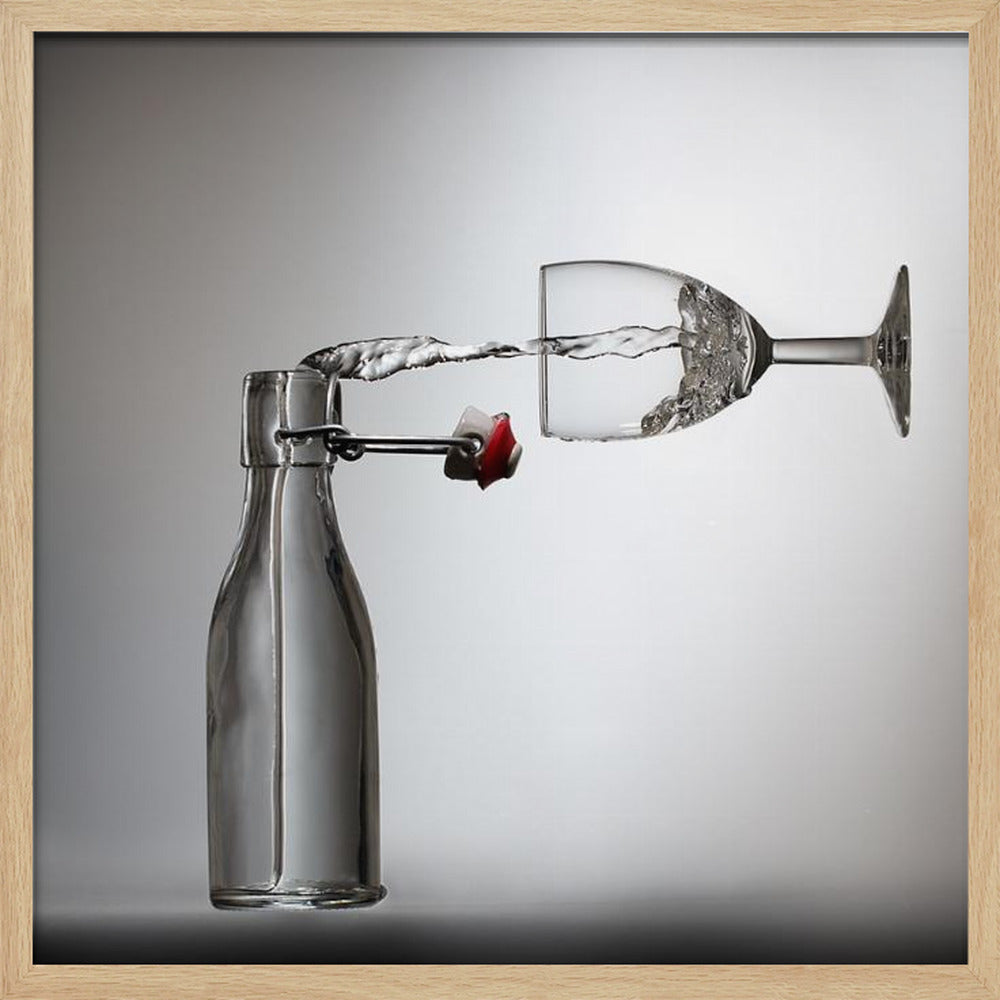 A conceptual photograph in a light wood frame depicting water pouring horizontally from an open swing-top glass bottle into a floating, sideways wine glass against a simple gray background, capturing the liquid in mid-air. Print