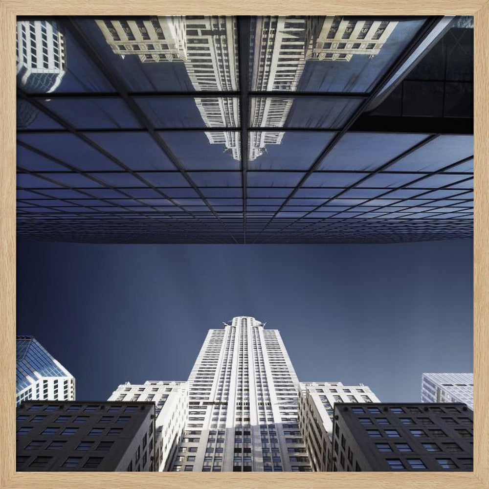 A framed, low-angle photograph capturing a stark white skyscraper against a deep blue sky, with its perfect reflection mirrored in the dark glass facade of an overhanging building, creating a surreal and symmetrical composition. Wall Art