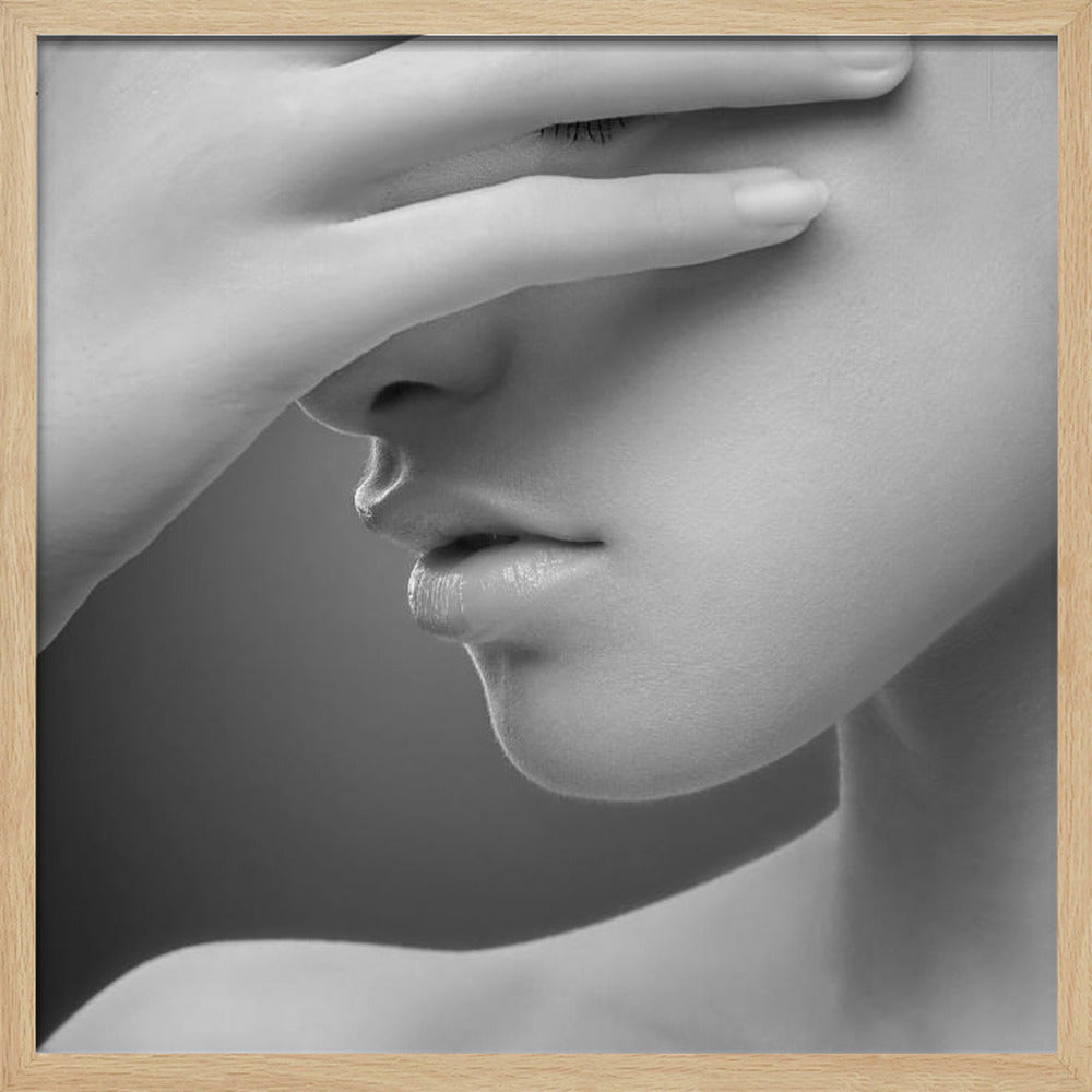 A close-up, black and white photograph of a woman's face. Her hand covers her eyes, revealing only the lower half of her face including her nose, lips, and chin. The image has a soft, sensual quality and is set within a light-colored wooden frame. Decor