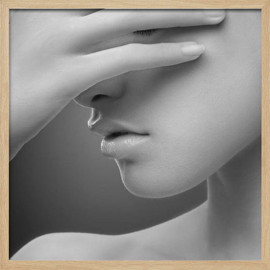 A close-up, black and white photograph of a woman's face. Her hand covers her eyes, revealing only the lower half of her face including her nose, lips, and chin. The image has a soft, sensual quality and is set within a light-colored wooden frame. Decor