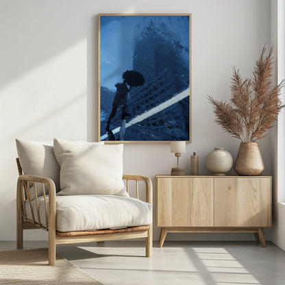 A moody, blue-toned photograph of a reflection in a rainy puddle. A black silhouette of a person holding an umbrella and a distorted brick building are visible, with a single white line crossing the wet street. Poster