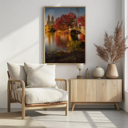 A picturesque autumn scene in Central Park featuring the Bow Bridge over a calm lake reflecting the vibrant red and yellow fall foliage, with the twin towers of The San Remo building visible in the background against a clear blue sky. Decor