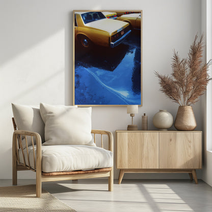A close-up, angled view of the rear of a yellow taxi cab on a wet street. The car's dark reflection is cast upon a large, vibrant blue puddle in the foreground, with visible ripples from the rain. Wall Art